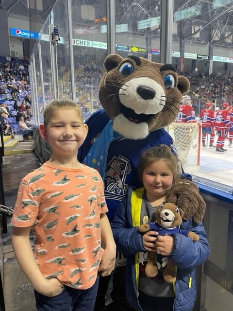 Two children posing with the Victoria Royals marmot mascot next to a hockey game