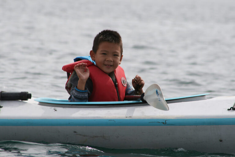 A young boy on the water sitting in a kayak waving