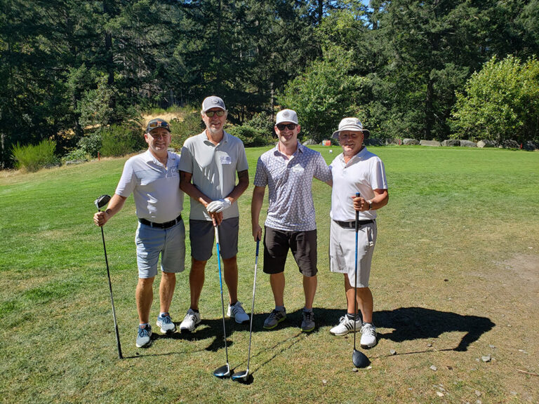 Four men posing at the IKCA Golf Tournament for a photo, with their clubs in hand